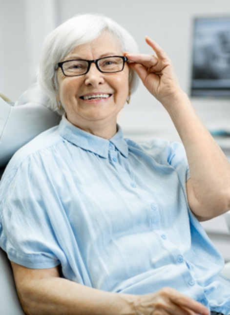 Senior woman with glasses sitting in dental chair and smiling